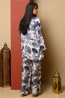 Woman wearing a blue and white patterned outfit standing against a beige wall with decorative lanterns.