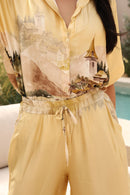 Person wearing a yellow outfit with a scenic print, standing by a poolside.