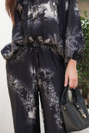 Person wearing a black and white patterned outfit holding a black handbag.