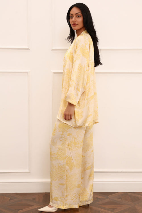 Woman wearing a yellow tie-dye outfit standing against a white paneled wall.