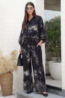 Woman in a black floral outfit standing on a staircase with plants in the background