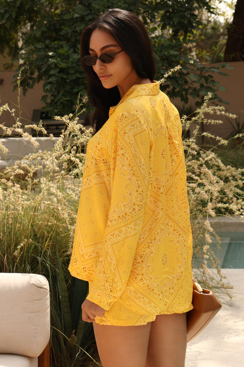 Woman wearing a yellow lace outfit with sunglasses outdoors.