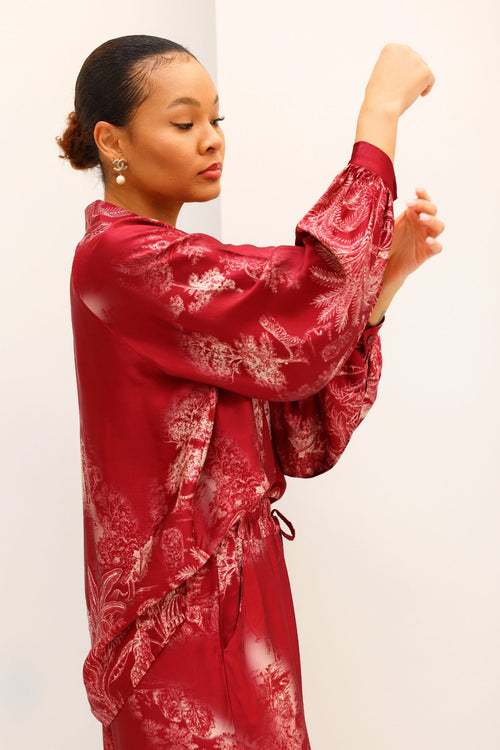 Woman wearing a red satin robe with white floral patterns against a plain background
