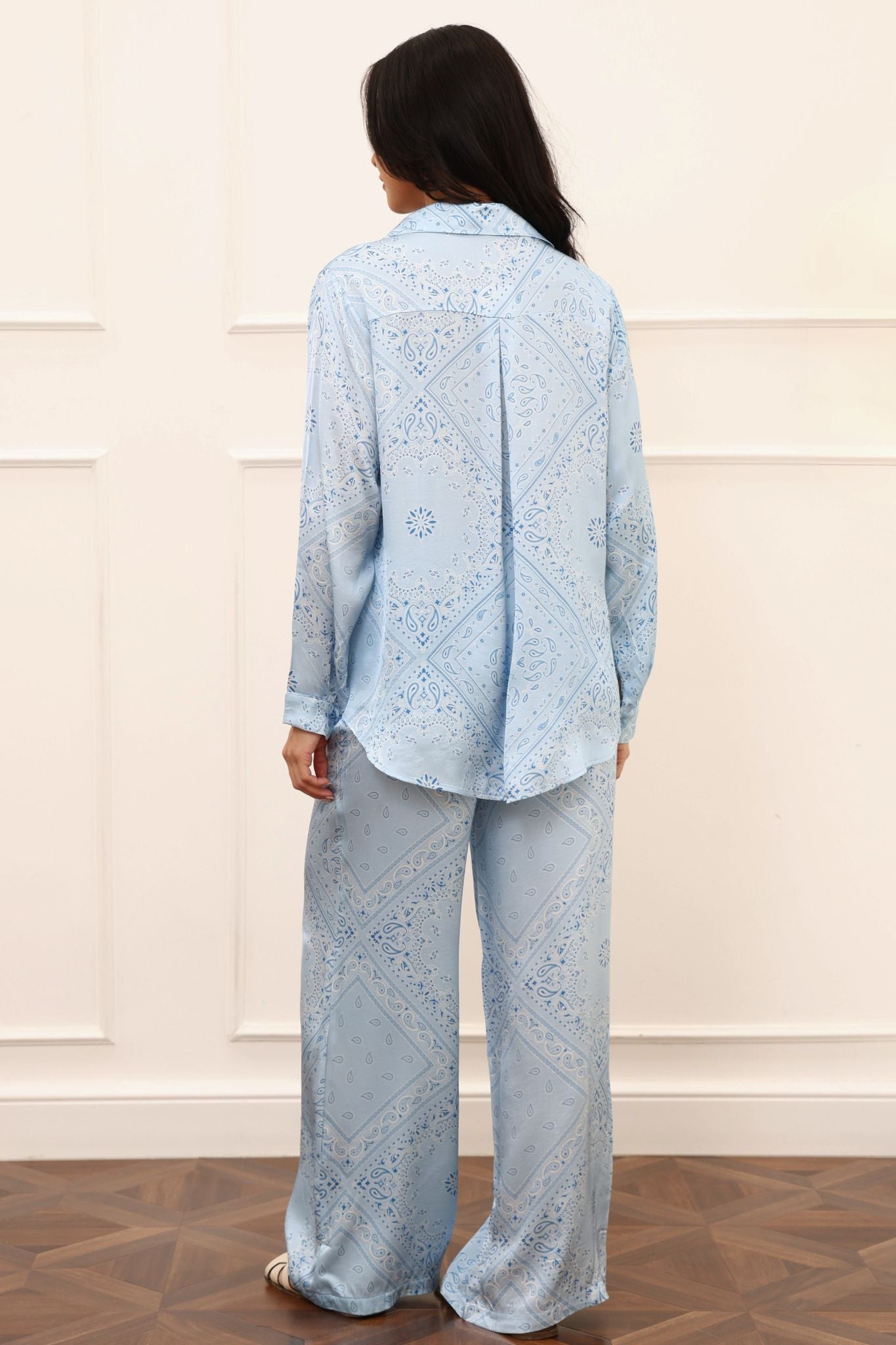 Woman wearing a light blue paisley outfit against a white wall.