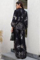 Woman wearing a black floral outfit standing against a white wall.