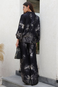 Woman wearing a black floral outfit standing against a white wall.