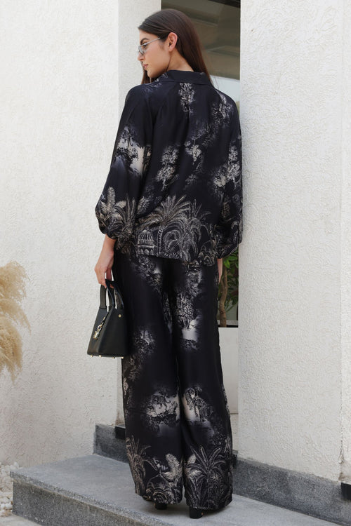 Woman wearing a black floral outfit standing against a white wall.