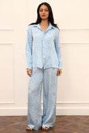 Woman wearing a light blue patterned outfit against a white wall.