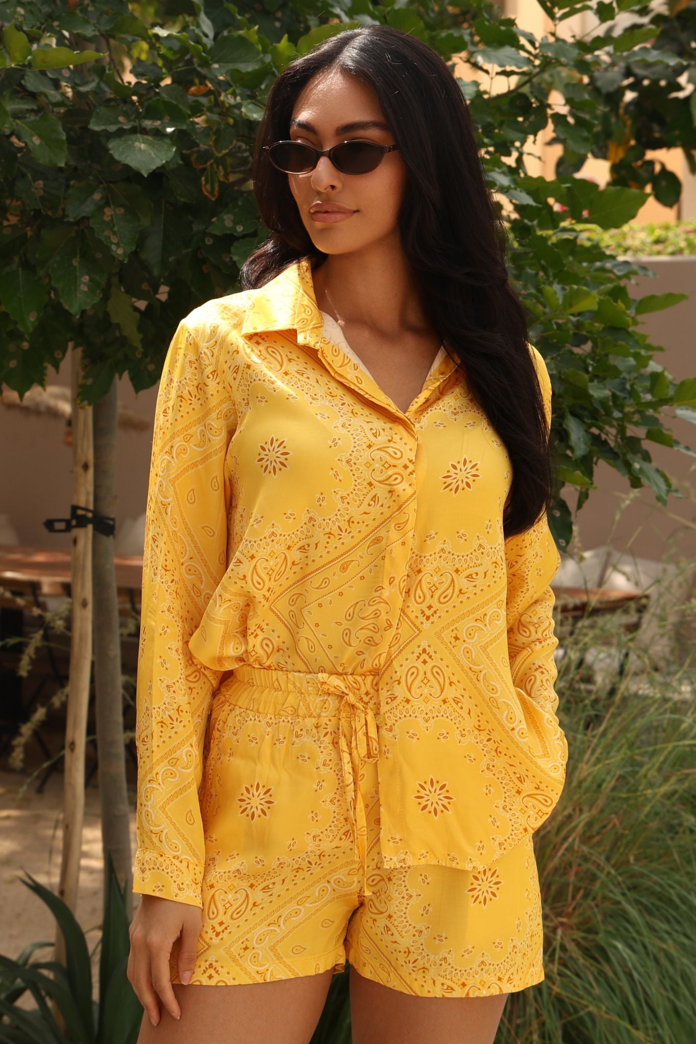 Woman wearing a yellow embroidered outfit with sunglasses outdoors.