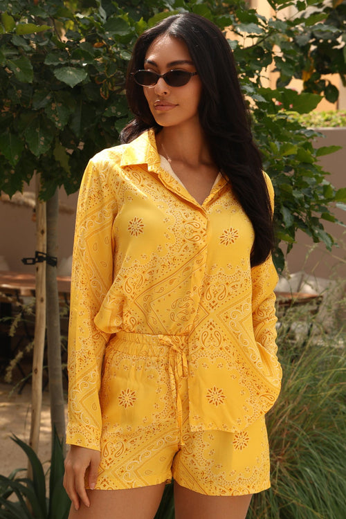 Woman wearing a yellow embroidered outfit with sunglasses outdoors.
