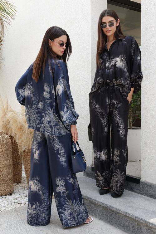 Two women wearing matching navy and black floral outfits standing outside a building.