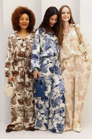 Three women wearing patterned outfits standing together against a white background