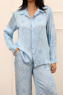Person wearing a light blue paisley shirt and pants against a beige background