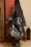 Woman wearing a black floral patterned outfit standing against a beige wall with decorative lanterns.