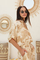 Woman in a gold patterned outfit standing outdoors with rattan wall design in the background