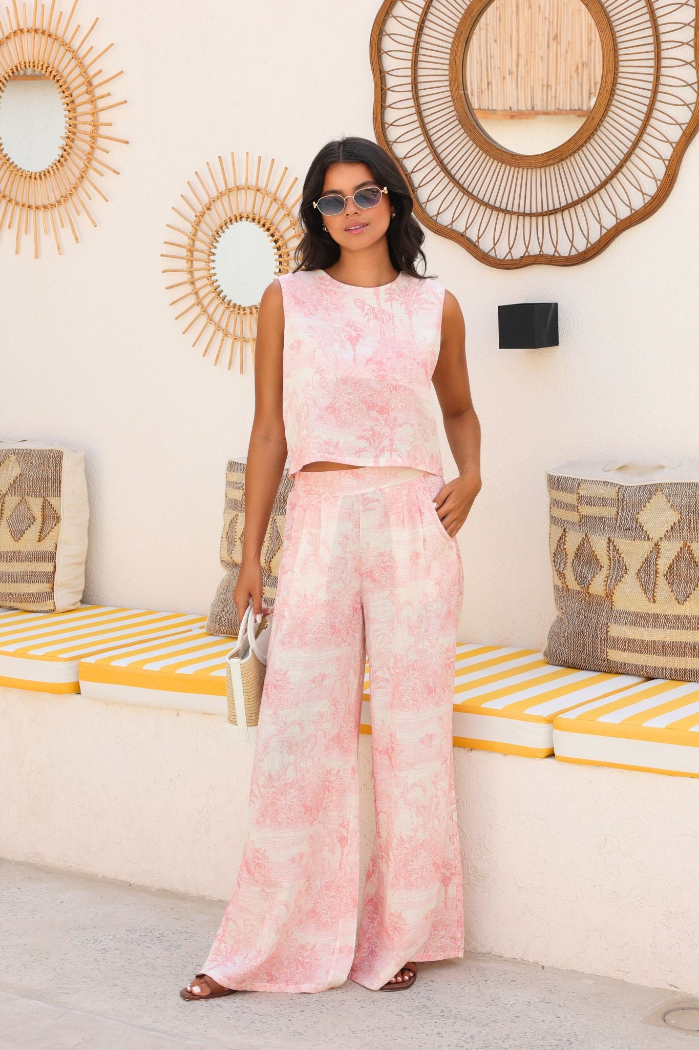 Woman in a pink tie-dye outfit standing in a room with decorative mirrors and striped cushions.
