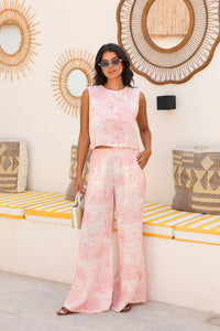 Woman in a pink tie-dye outfit standing in a room with decorative mirrors and striped cushions.