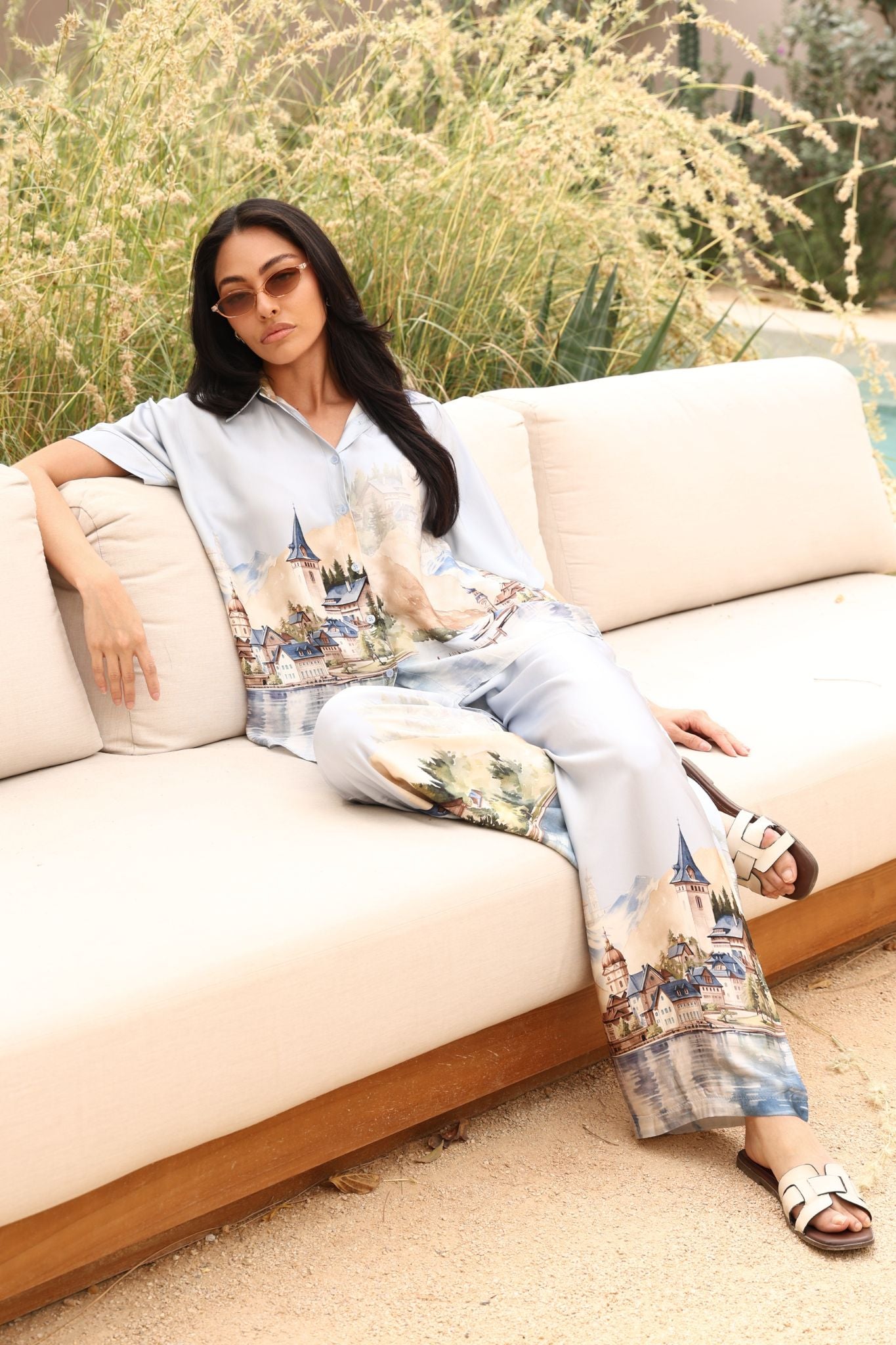 Woman sitting on a beige sofa outdoors with greenery in the background