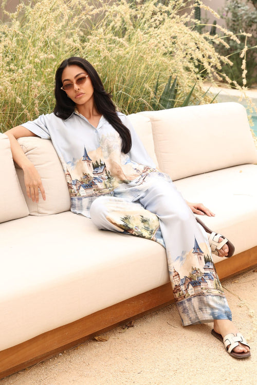 Woman sitting on a beige sofa outdoors with greenery in the background