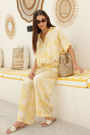 Woman in a yellow patterned outfit sitting outdoors with beige handbag
