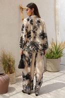 Woman wearing a floral outfit standing in a sunlit outdoor space with plants.