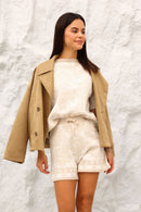 Woman wearing a beige coat over a white outfit against a textured white background