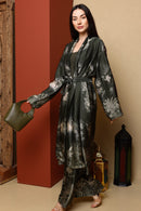 Woman wearing a long, patterned robe holding a green handbag against a warm-toned wall.