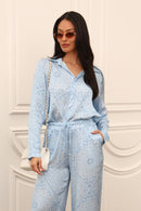 Woman wearing a light blue paisley set against a white wall.