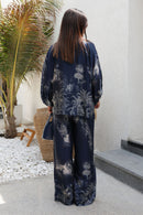 Person wearing a navy floral outfit standing in a modern outdoor setting with a palm tree.