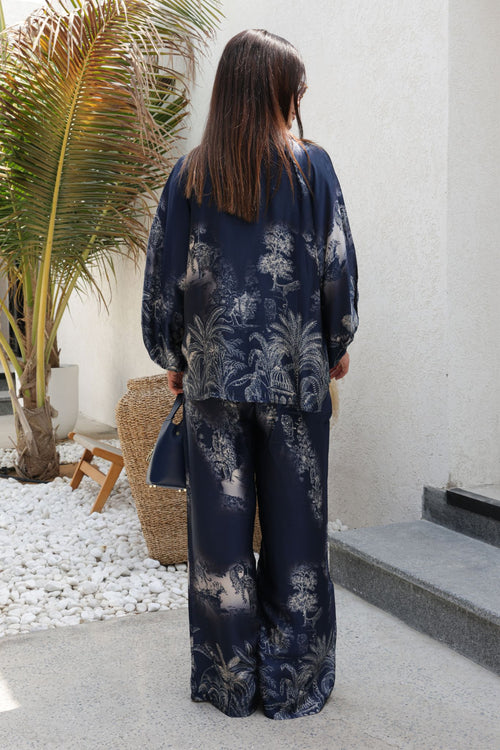 Person wearing a navy floral outfit standing in a modern outdoor setting with a palm tree.