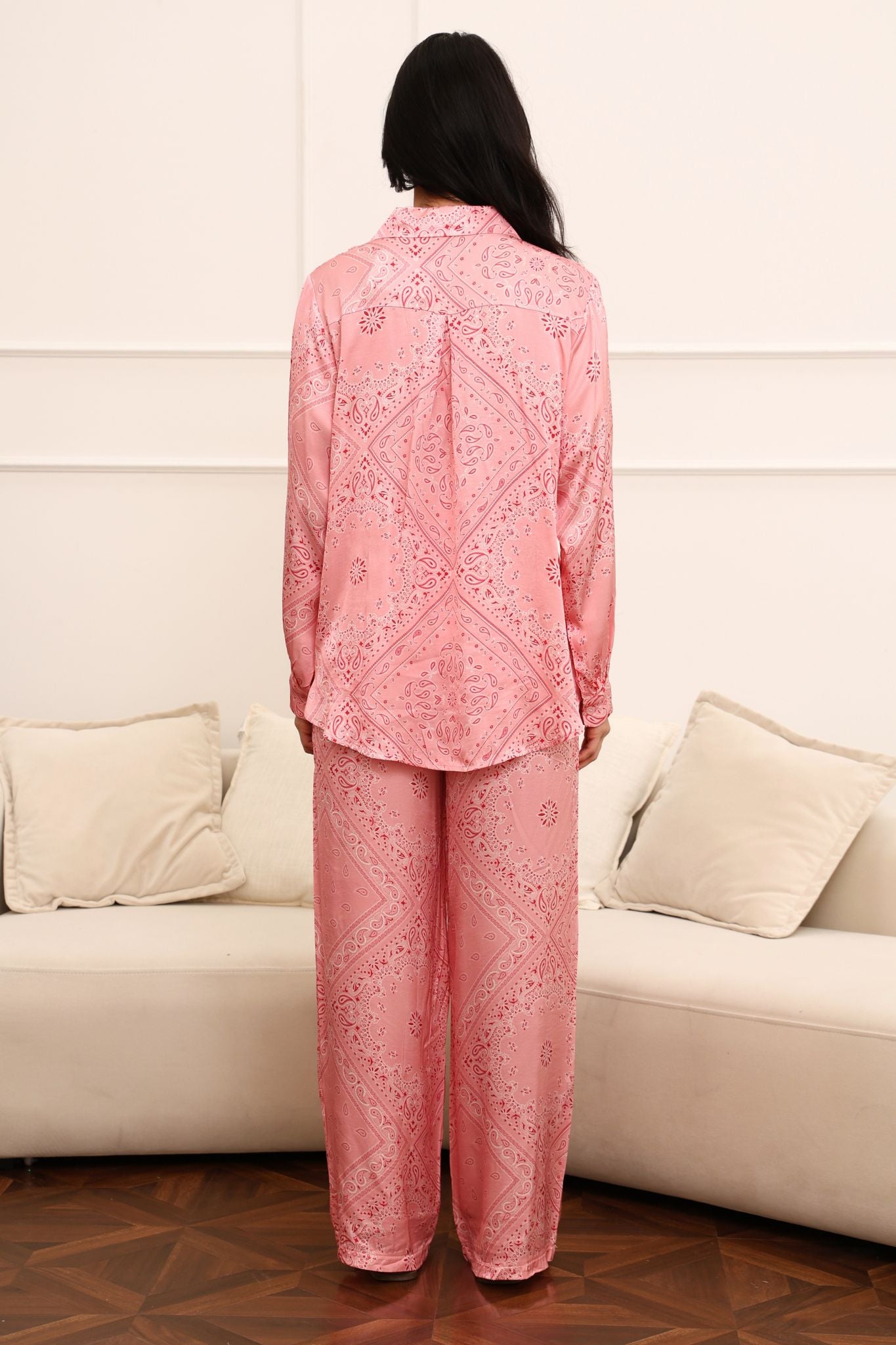 Person wearing a pink paisley outfit standing in front of a white couch.