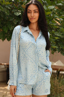 Woman wearing a light blue patterned outfit standing outdoors with greenery in the background