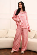 Woman wearing pink paisley set sitting on a white couch.