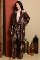 Woman wearing a brown floral kimono-style outfit standing against a beige wall with decorative lanterns.