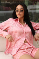 Woman wearing a pink patterned outfit sitting on a couch.