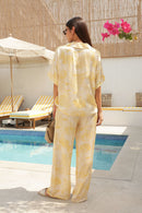 Woman in a yellow patterned outfit standing outdoors with pool in the background