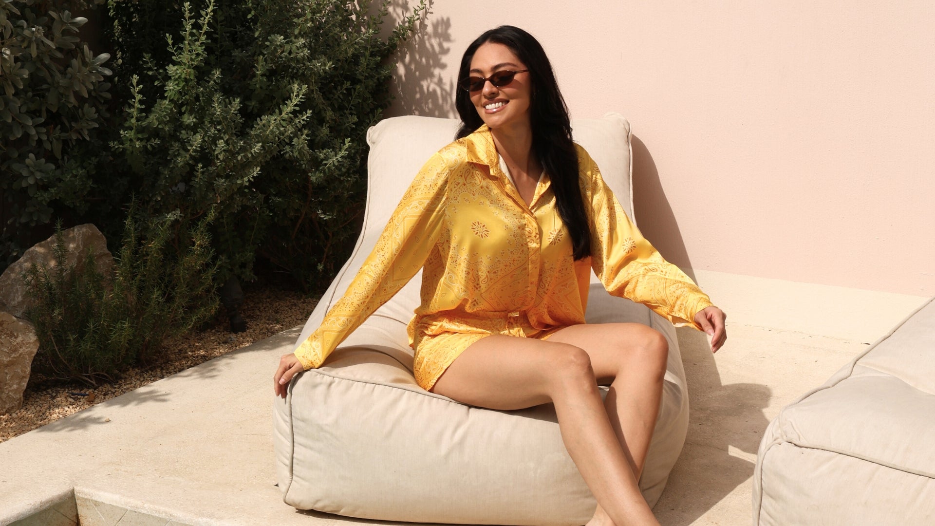 Woman in a yellow shirt sitting on a beige chair outdoors.