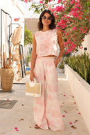 Woman in a pink outfit standing in a garden with flowers and plants.