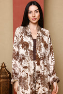 Woman wearing a patterned long-sleeve top against a beige wall.