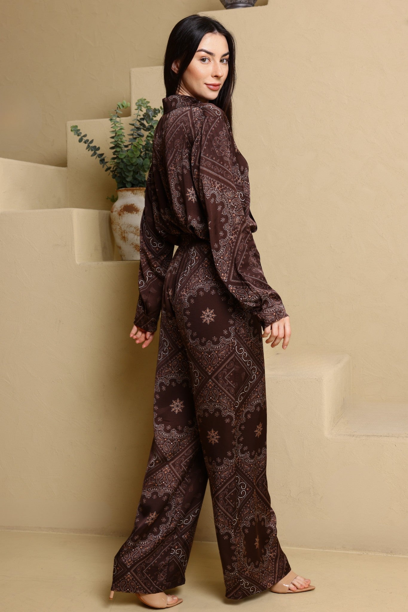 Woman wearing a brown patterned outfit standing in a minimalistic room.