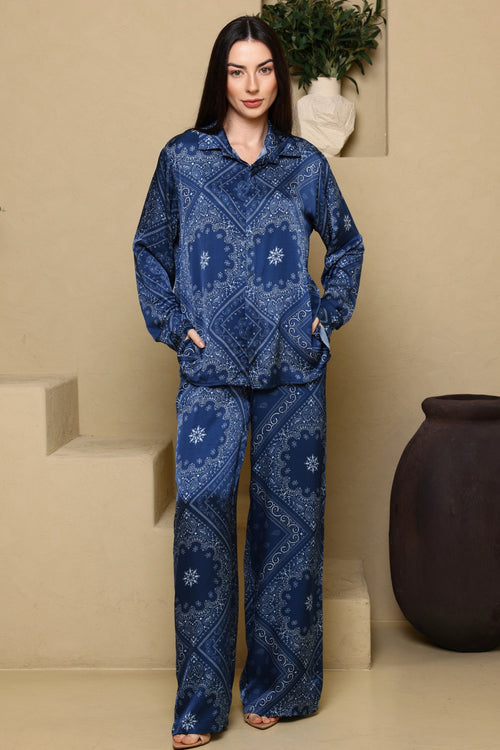 Woman wearing a blue patterned outfit standing against a beige wall with decorative elements.