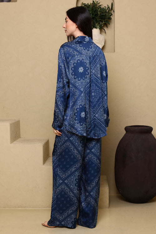 Woman wearing a blue patterned outfit standing in a room with beige walls and a dark vase.