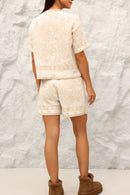 Person wearing a white textured outfit with brown boots against a textured white background