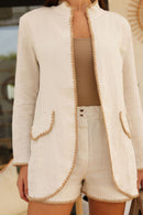 Person wearing a beige linen blazer with white trim and matching shorts.
