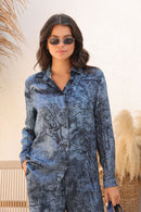 Woman wearing a blue patterned outfit with sunglasses against a neutral background