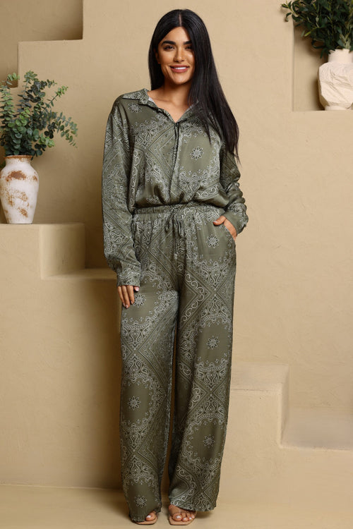 Woman wearing a green patterned outfit standing in a minimalistic setting with beige steps and decorative vases.