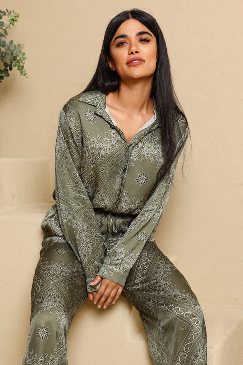 Woman wearing a green patterned outfit sitting on a beige chair.