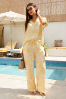Woman in a yellow patterned outfit standing outdoors with pool in the background