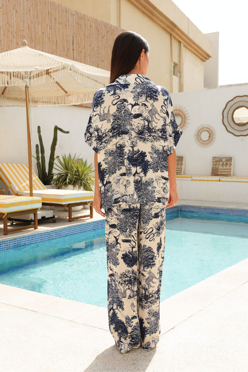 Woman in a navy patterned outfit standing outdoors with pool in the background