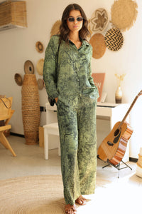 Woman in a green patterned outfit standing in a room with decorative items on the wall.